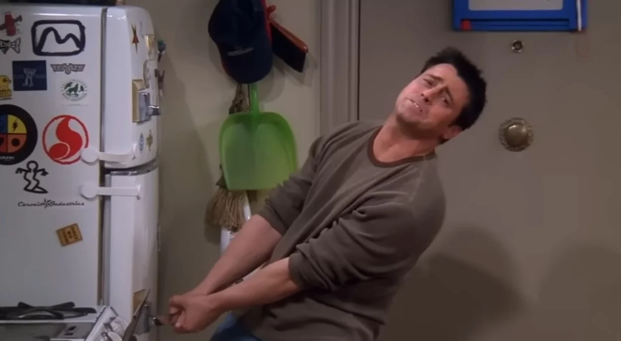 Joey Tribbiani struggling to open a baby-proofed fridge in Friends.